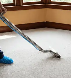 Steam carpet cleaning technician using a hot-water extraction wand on a residential carpet, wearing blue protective shoe covers Dover, DE.